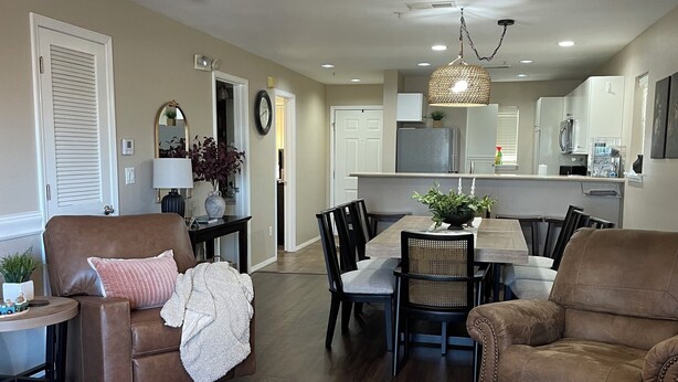 A spacious living room with a brown leather sofa, a wooden coffee table with a plant, and a dining area with a chandelier.