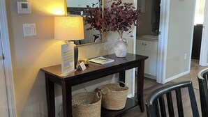 A wooden console table with a lamp, a mirror, and a vase with flowers. There are two woven baskets on the floor.