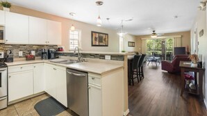 A modern kitchen with a central island, a dining area with a table and chairs, and a view of the outdoors through large windows.