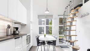 Une cuisine moderne avec des meubles blancs, un coin repas doté d’une table ronde et de chaises, et un escalier avec des marches en bois et des rampes en métal.
