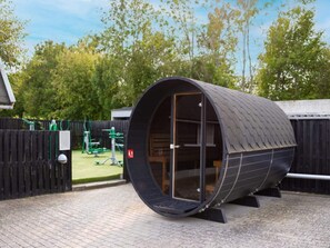 Una estructura cilíndrica y moderna con techo curvo, posiblemente un hotel cápsula o un alojamiento singular, ubicada en una zona ajardinada con valla de madera y vegetación al fondo.