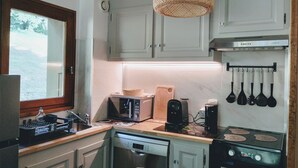 Una cocina compacta con armarios blancos, microondas integrado, tostadora, cafetera y estufa.