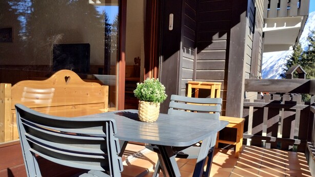 Un patio con una mesa, sillas, una planta en maceta y una valla de madera.