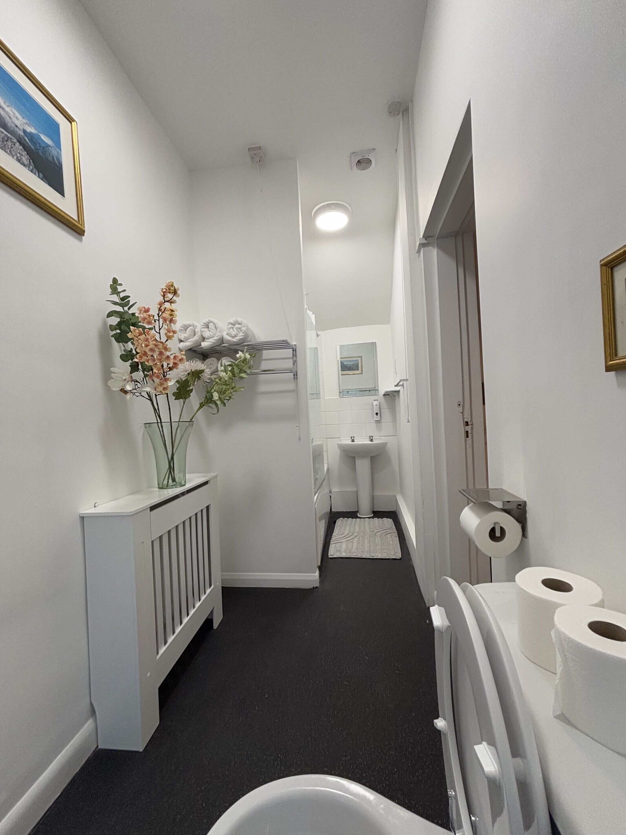 Een smalle gang met een radiator, een wastafel en toiletpapier aan de rechterkant.