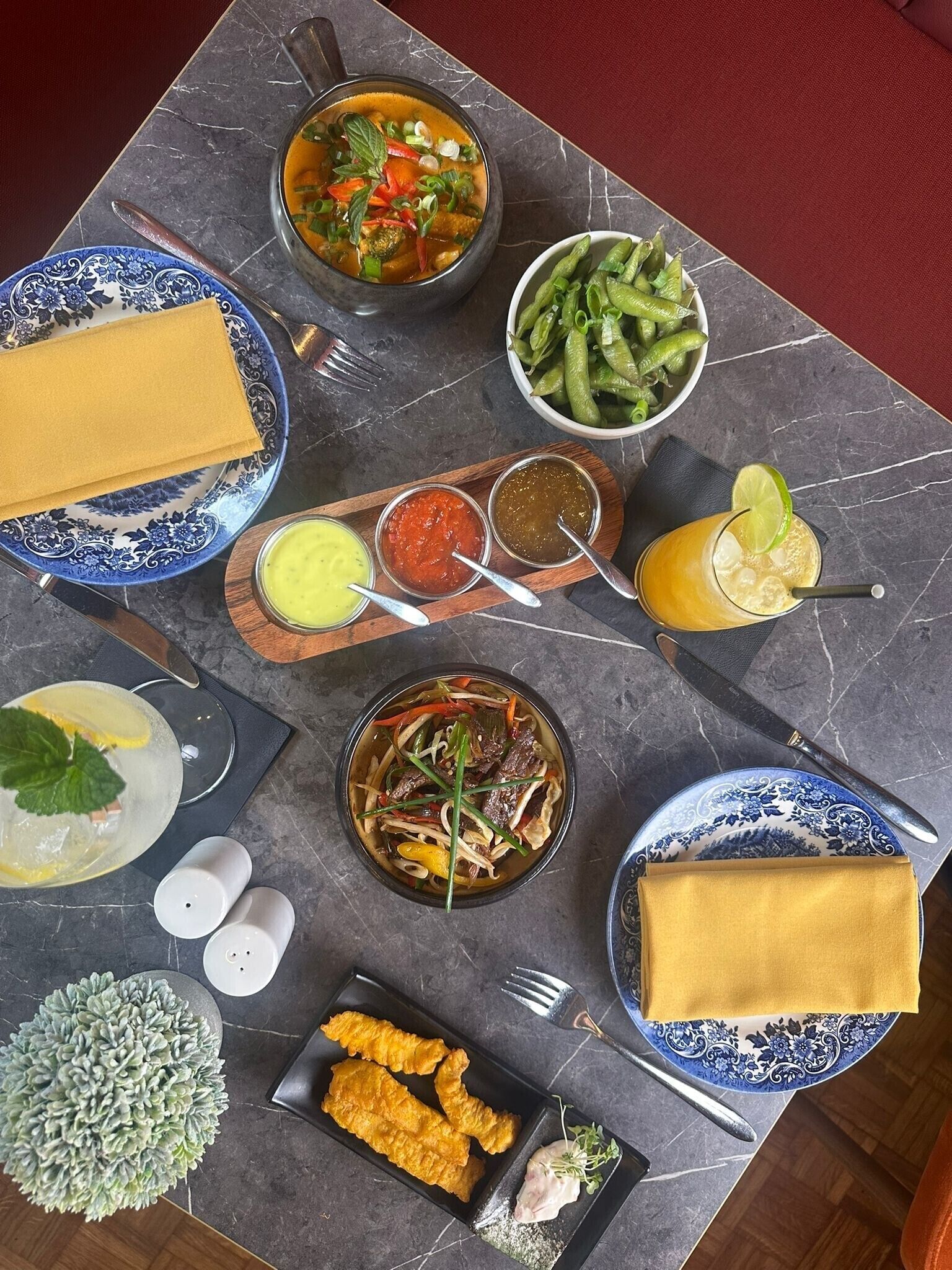 A table set with various dishes including soup, salad, and fried items, along with condiments and a drink.