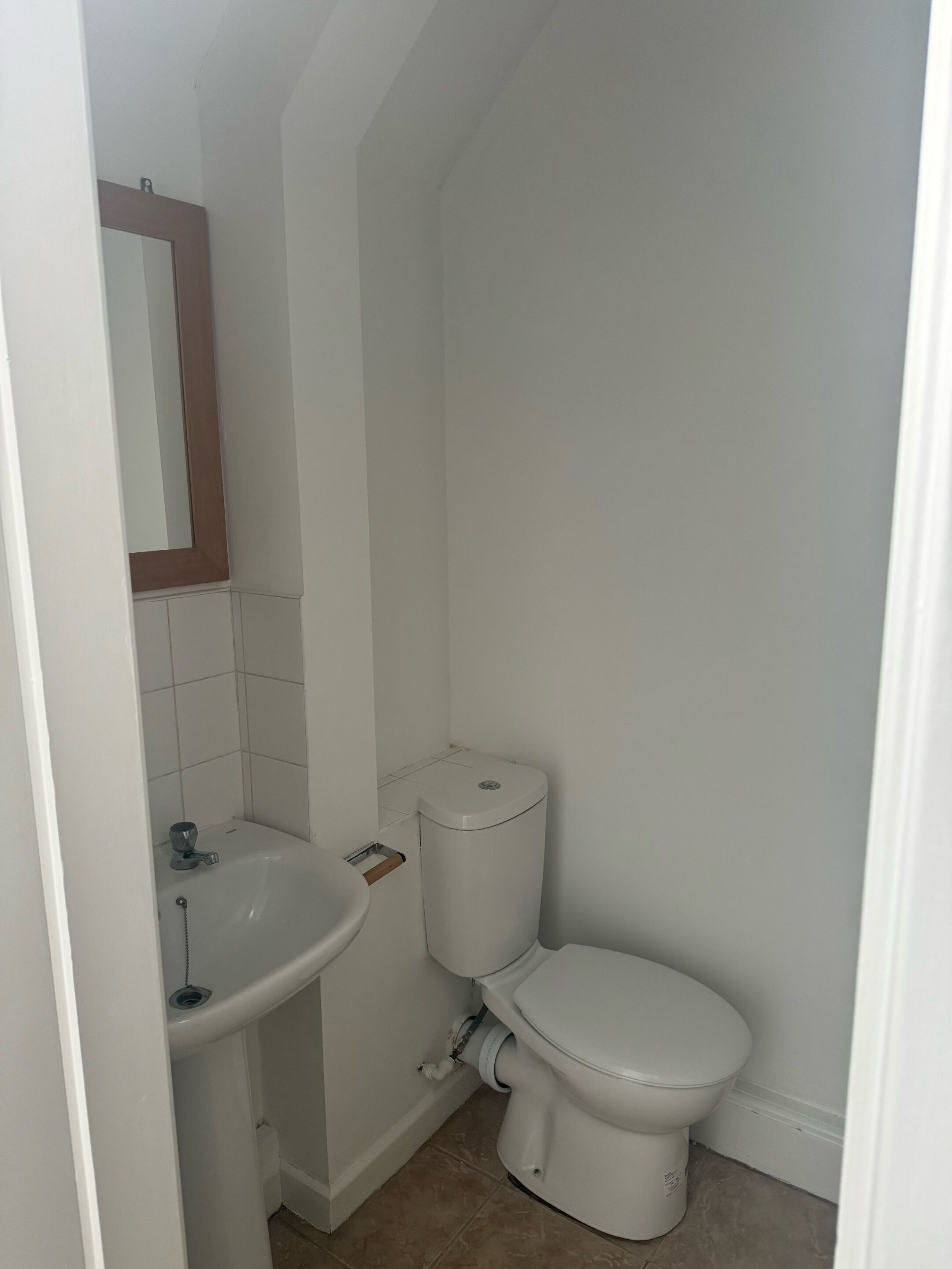 Un baño pequeño y limpio con lavamanos, inodoro y espejo blancos.