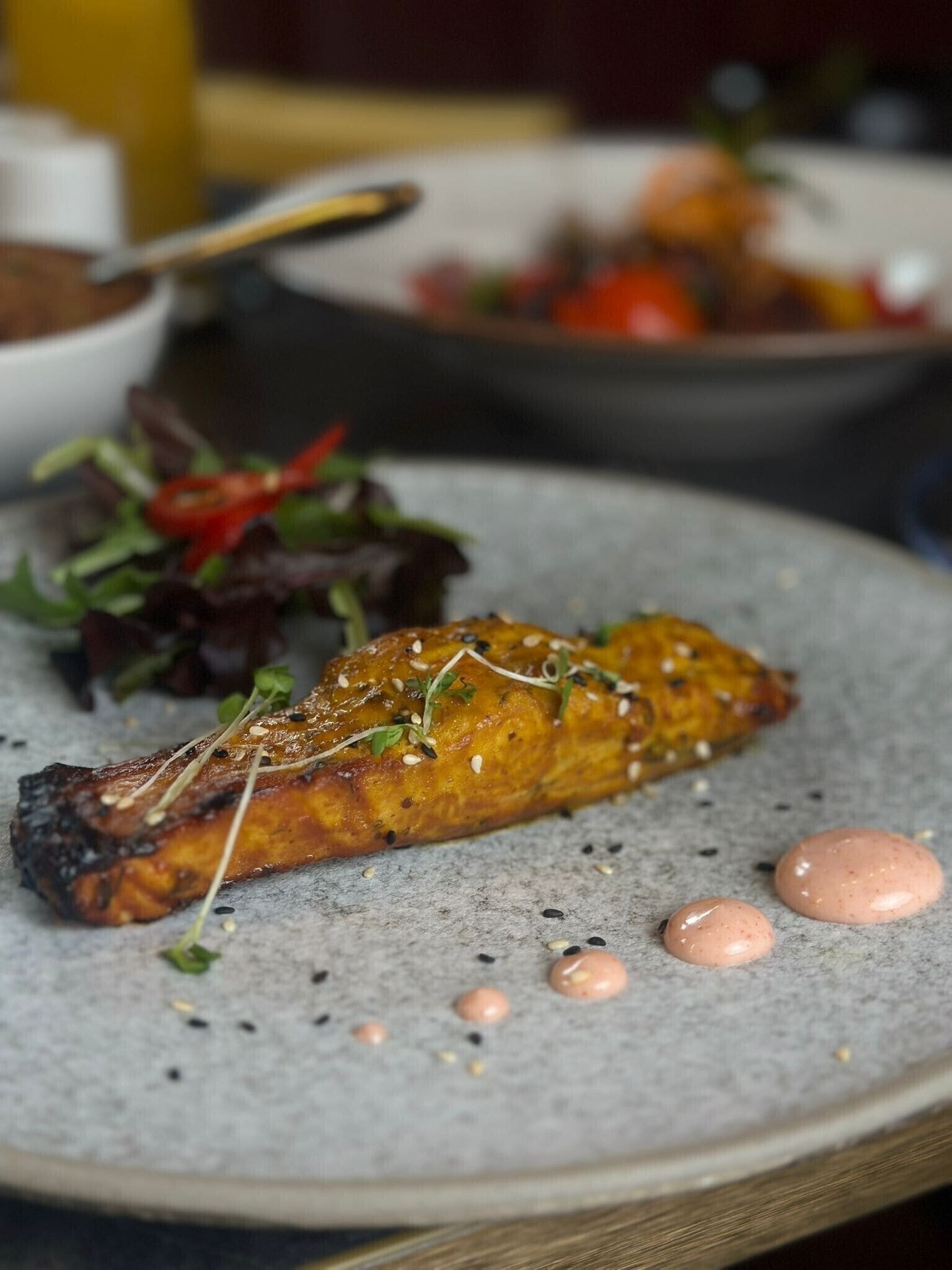 Ein Teller mit gegrilltem Lachs, einem gemischten Salat und zwei Klecksen Soße.