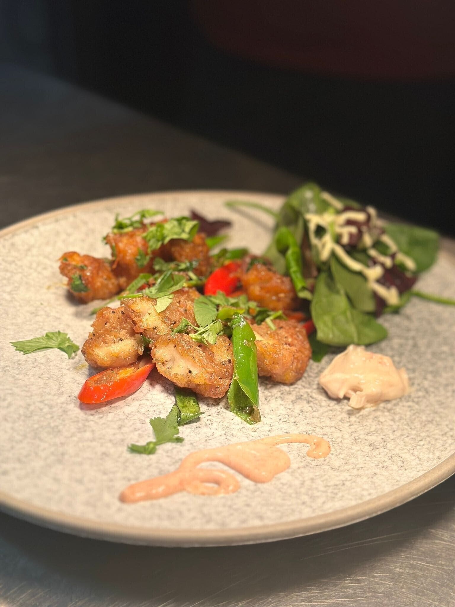 A plate of food with fried items, greens, and a sauce.