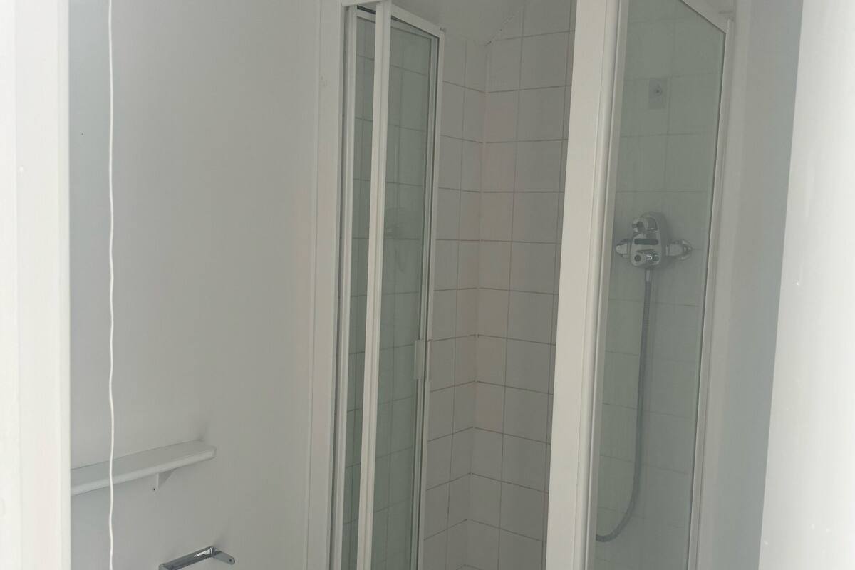 A small, enclosed shower area with a glass door, a white tiled wall, and a metal handle.