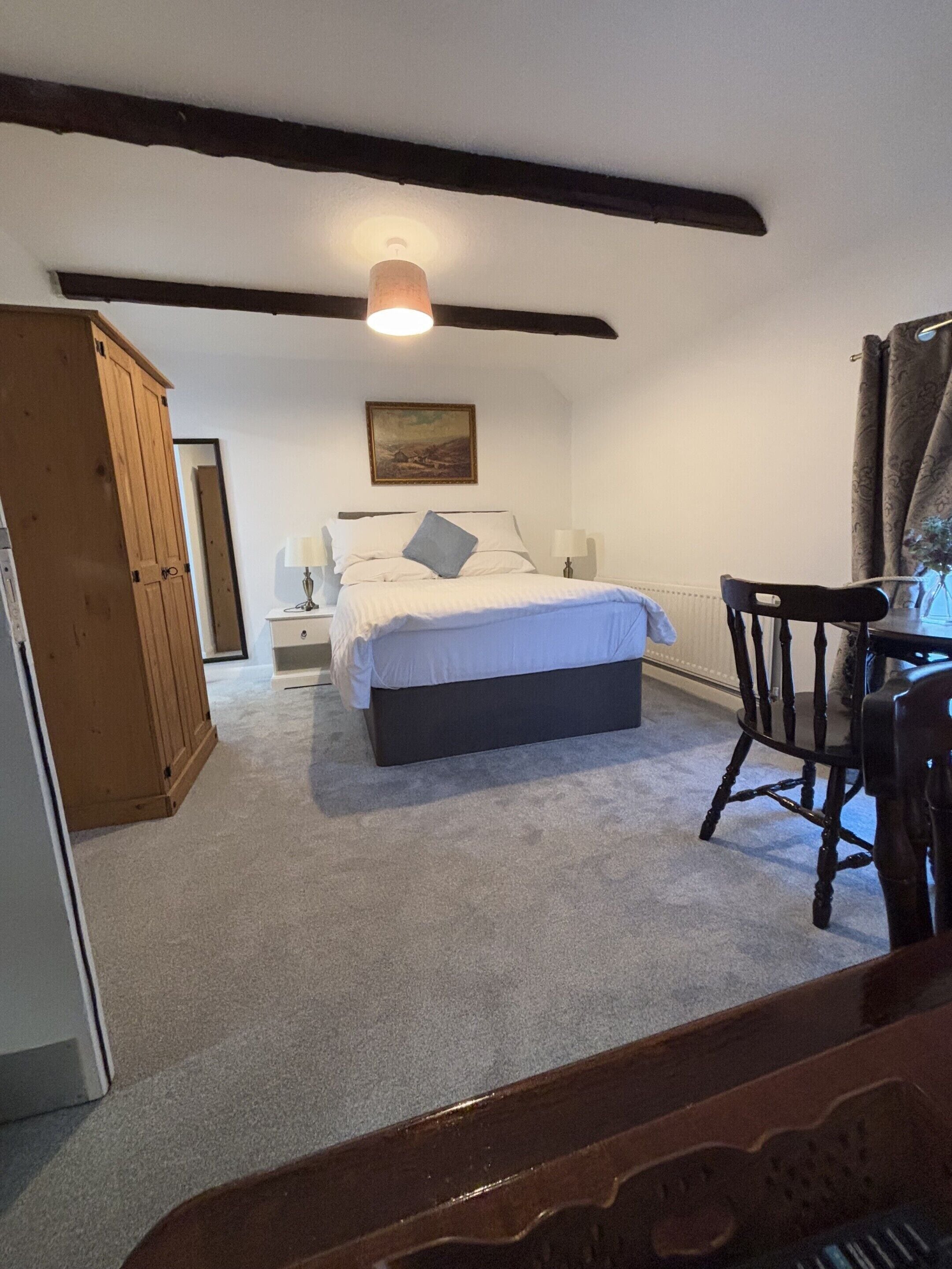 Une chambre à coucher avec un lit, des tables de chevet, une armoire en bois, une chaise et un tableau accroché au mur.