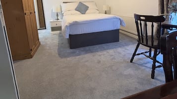 Un dormitorio con una cama, mesitas de noche, un armario de madera, una silla y un cuadro en la pared.