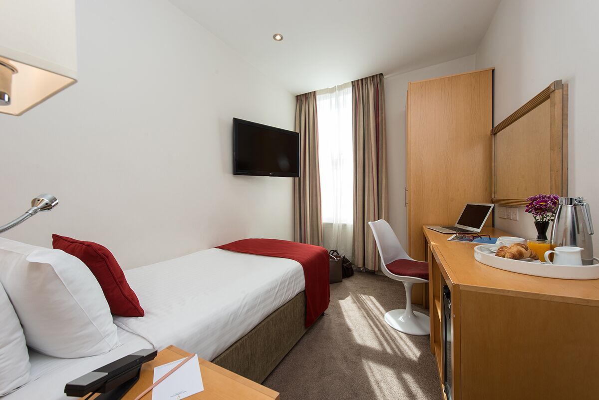 Une chambre d’hôtel comprenant un lit, un bureau avec un ordinateur portable, une chaise, une télévision et un plateau de petit-déjeuner.