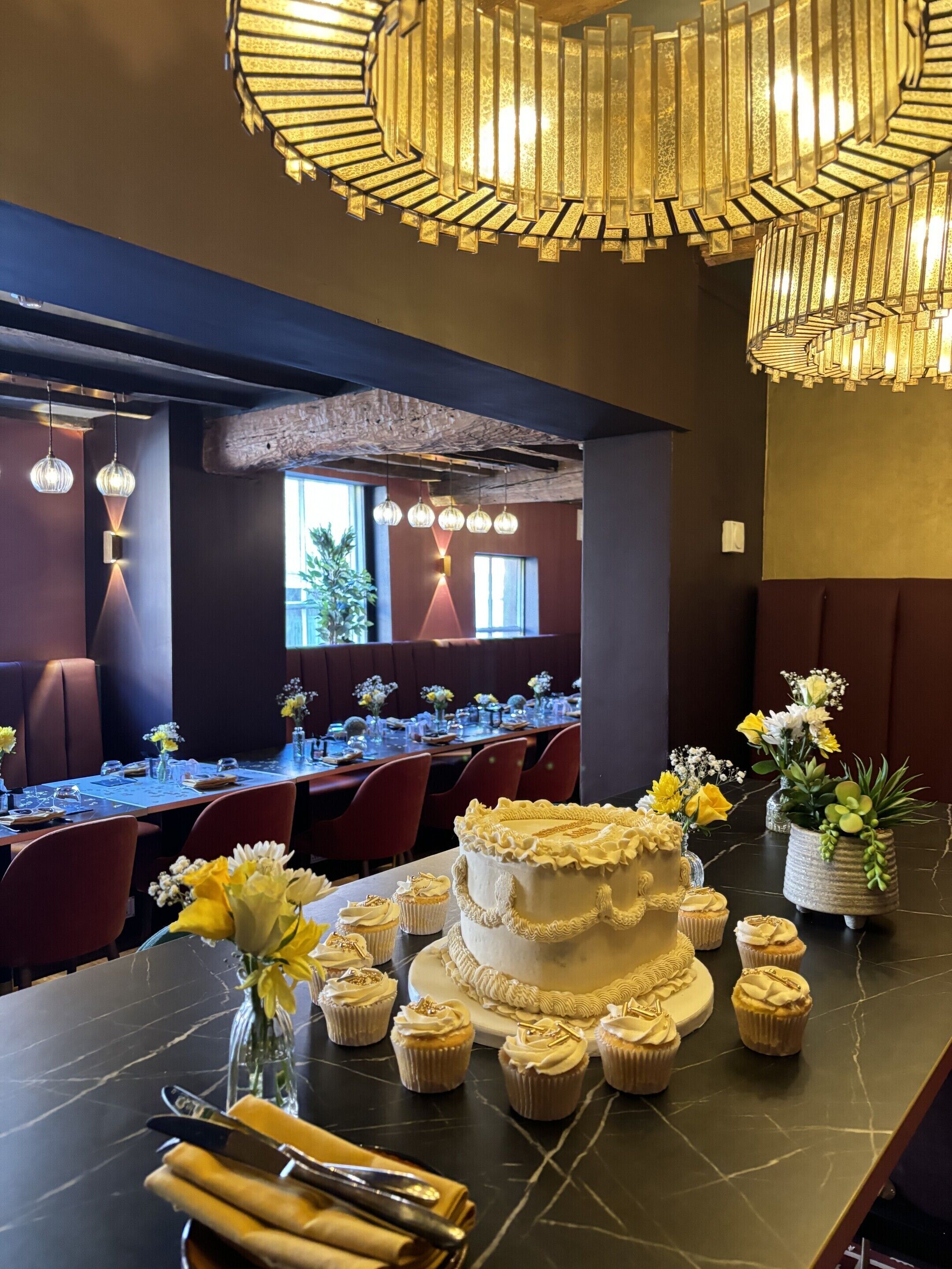 A dining area with a marble table, multiple chairs, a large cake, cupcakes, and floral centerpieces.
