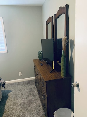 A bedroom with a wooden dresser, a television, and a mirror.