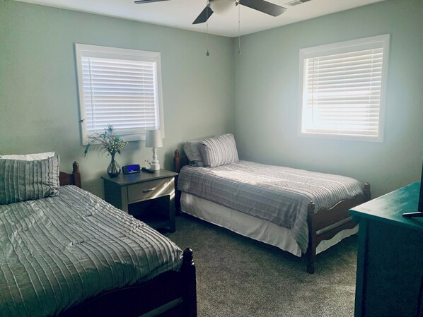 Une chambre avec deux lits, une table de chevet, un bureau et deux fenêtres équipées de stores.