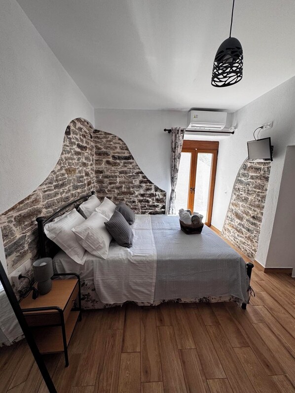 Un dormitorio con pared de piedra, una cama con almohadas, una mesita de noche, una lámpara, una silla y un aplique.