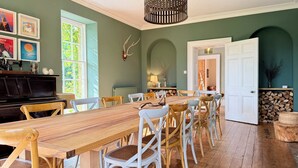 A dining area with a wooden table and chairs, a piano, and framed artwork on the wall. - Georgian Country House Secluded in 4 Acres, Hot Tubs & 8 Large En-Suite Bedrooms (Kentisbury)