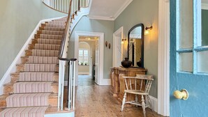 A grand staircase with a wooden finish and striped carpet, leading to a hallway with a blue door and a wooden console table. - Georgian Country House Secluded in 4 Acres, Hot Tubs & 8 Large En-Suite Bedrooms (Kentisbury)