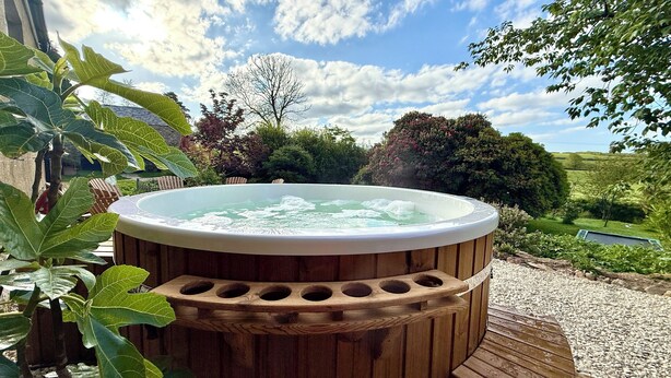A wooden hot tub surrounded by greenery, with a clear sky and a view of the countryside. - Georgian Country House Secluded in 4 Acres, Hot Tubs & 8 Large En-Suite Bedrooms (Kentisbury)