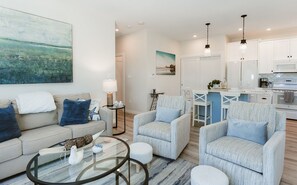 Un salon moderne avec un canapé, des fauteuils, une table basse et un coin cuisine à l’arrière-plan.