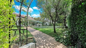 A brick pathway leading to a house with a red roof, surrounded by lush greenery and trees.