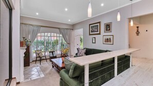 A living room with a green sofa, a white coffee table, and a dining area with a table and chairs. There are pendant lights, a fireplace, and framed pictures on the wall.