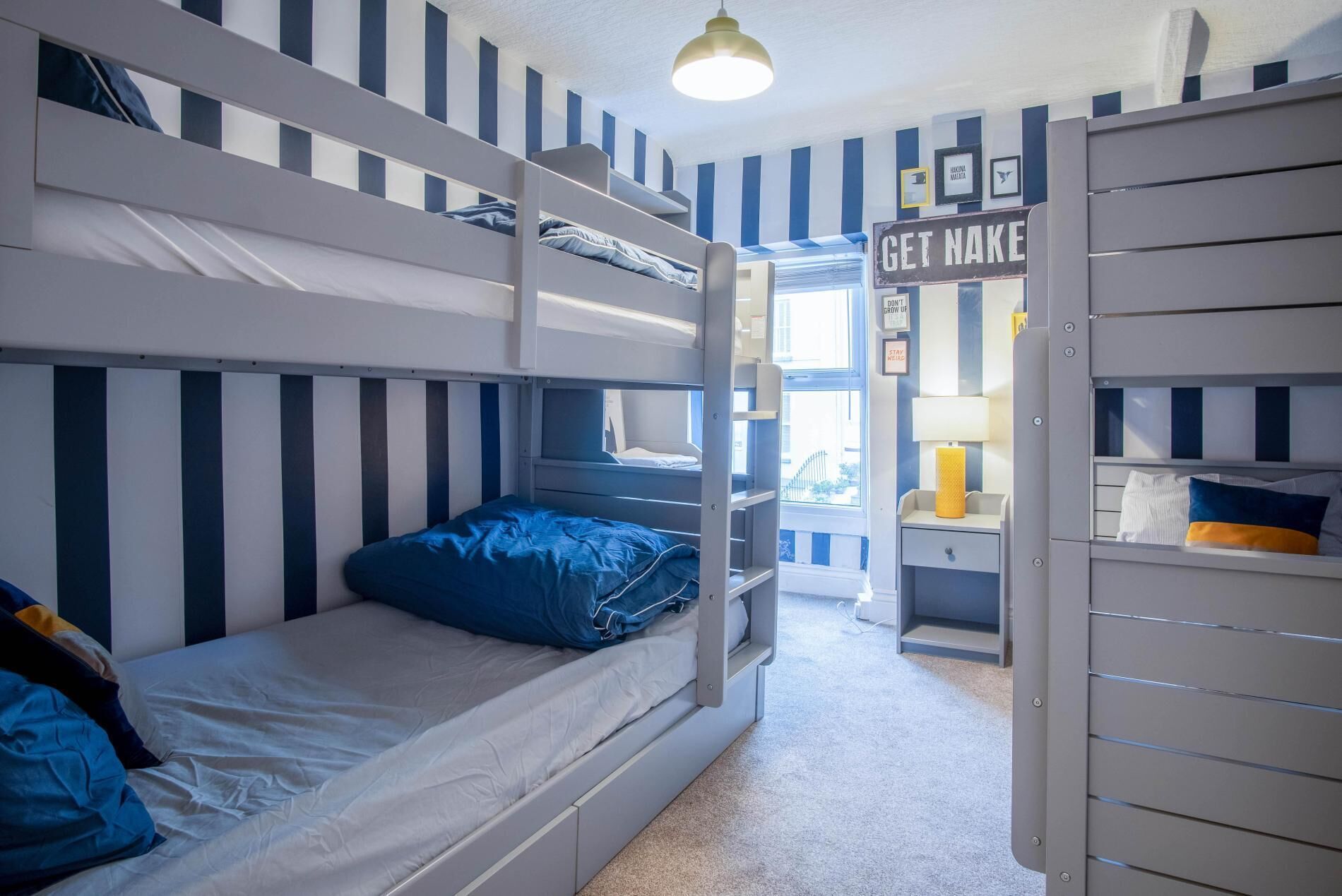 A bunk bed room with striped walls, a sign reading "GET NAKED", and a window with a view.