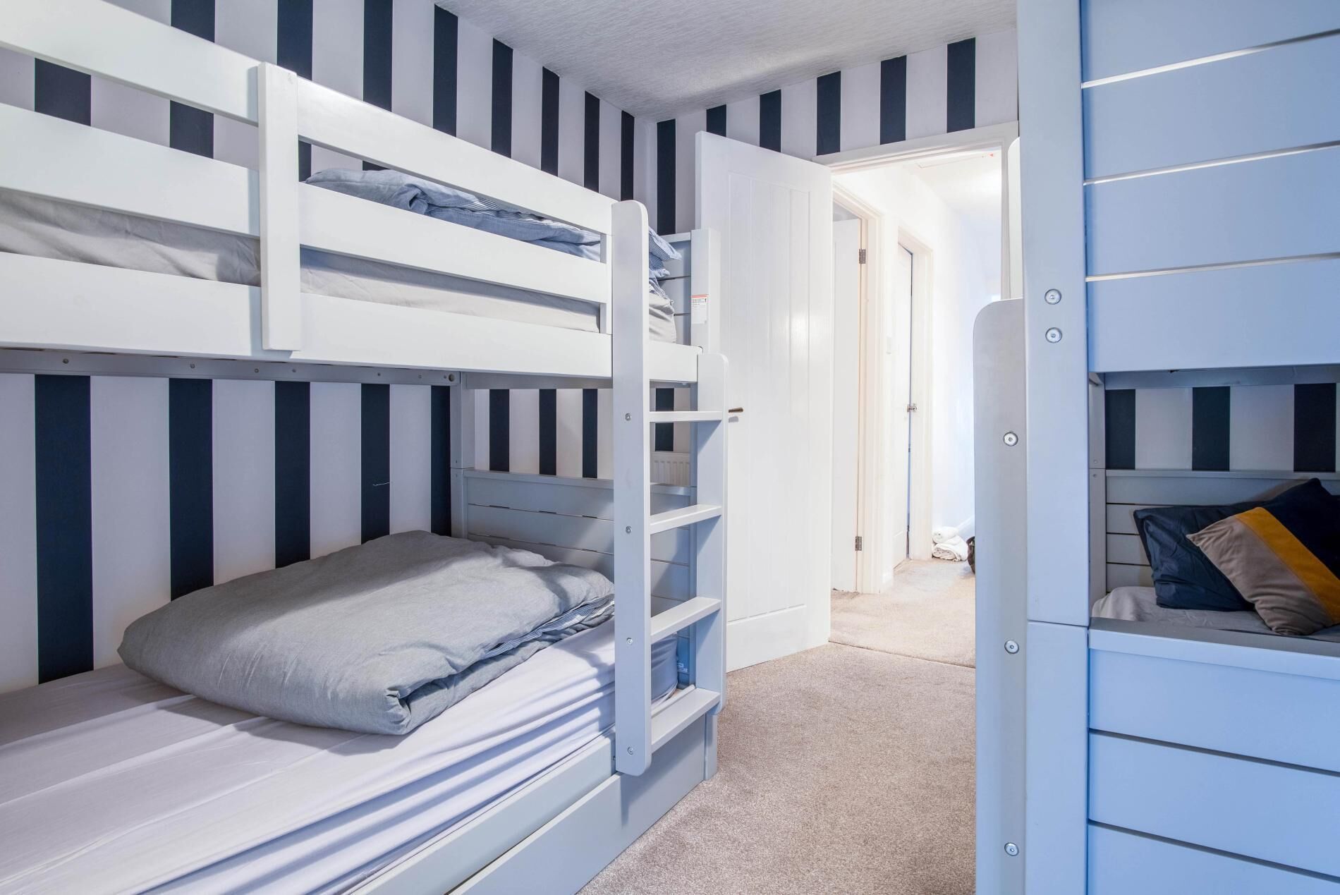A bunk bed room with striped walls, a door leading to another room, and a small closet with a mirror.