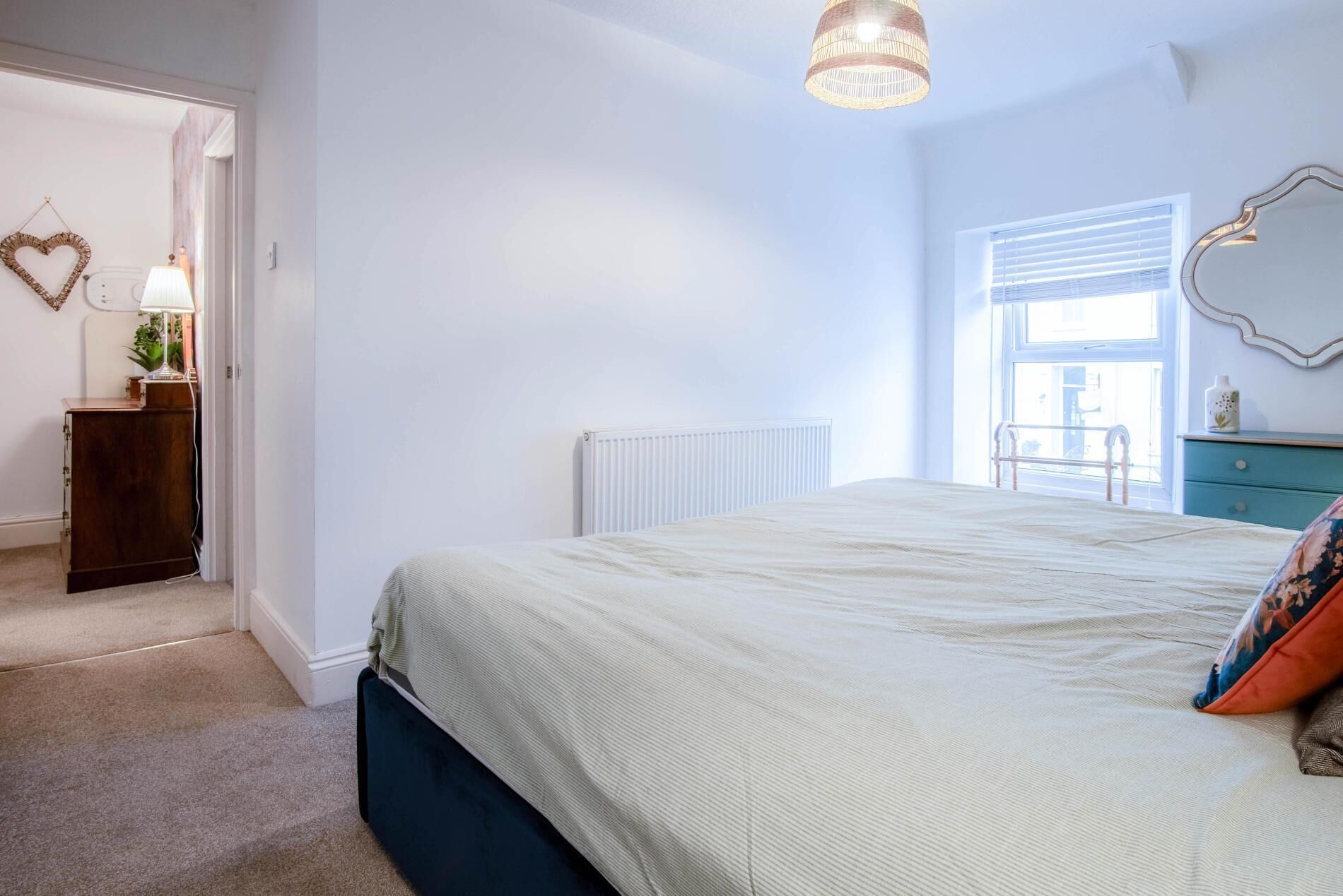 A bedroom with a bed, a dresser, a radiator, a window, and a hanging light fixture.