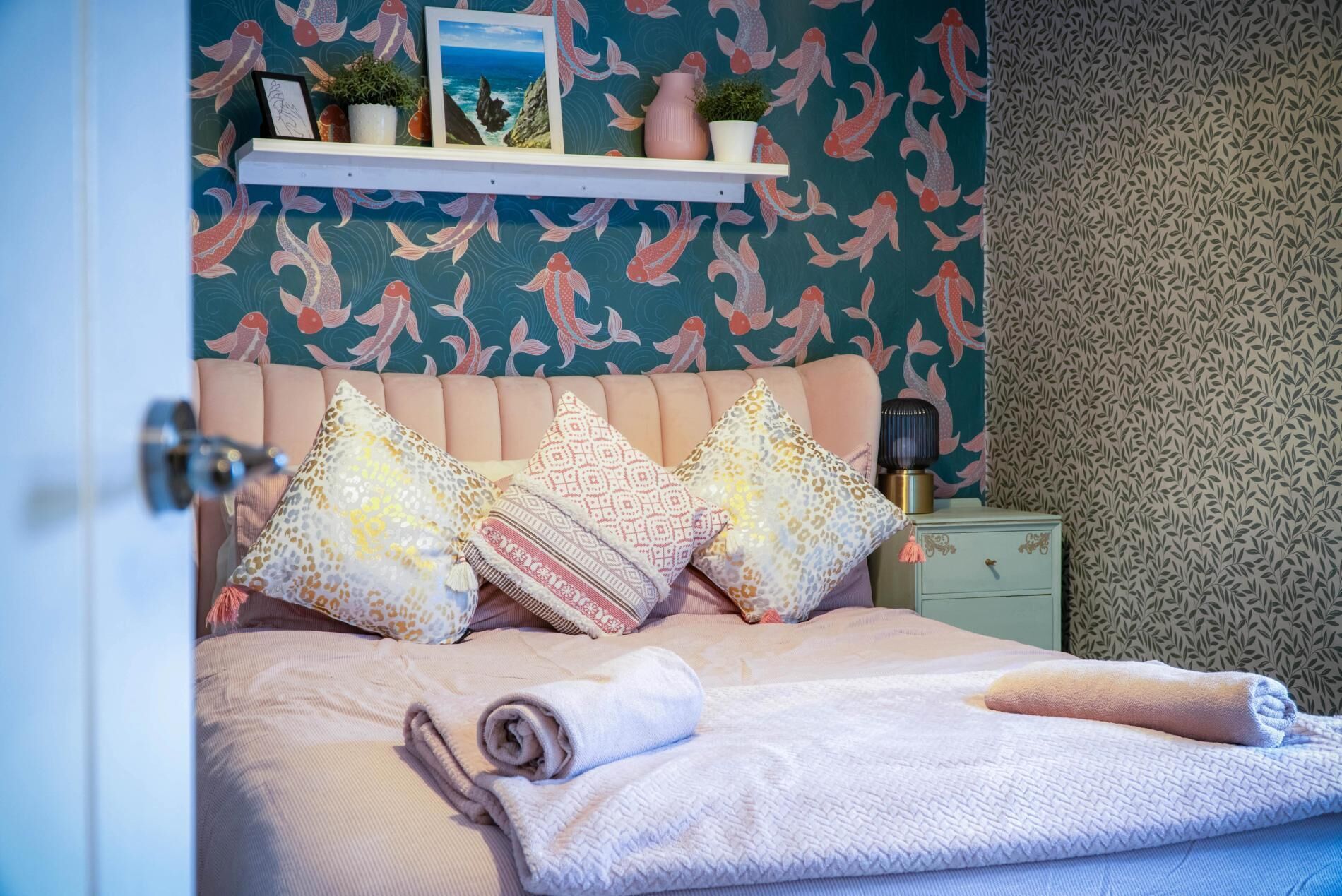 A bedroom with a bed, pillows, a bedside table, a nightstand, and a wall with a fish pattern.