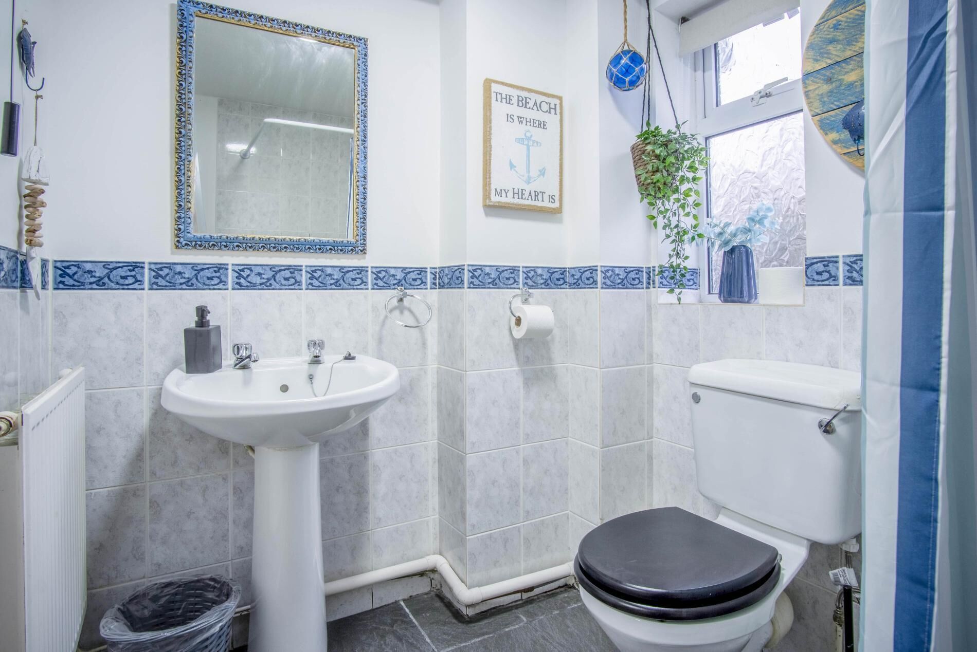 A bathroom with a white sink, a toilet, and a shower. There is a framed sign on the wall that says "The beach is where my heart is."