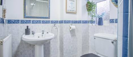 A bathroom with a white sink, a toilet, and a shower. There is a framed sign on the wall that says "The beach is where my heart is."