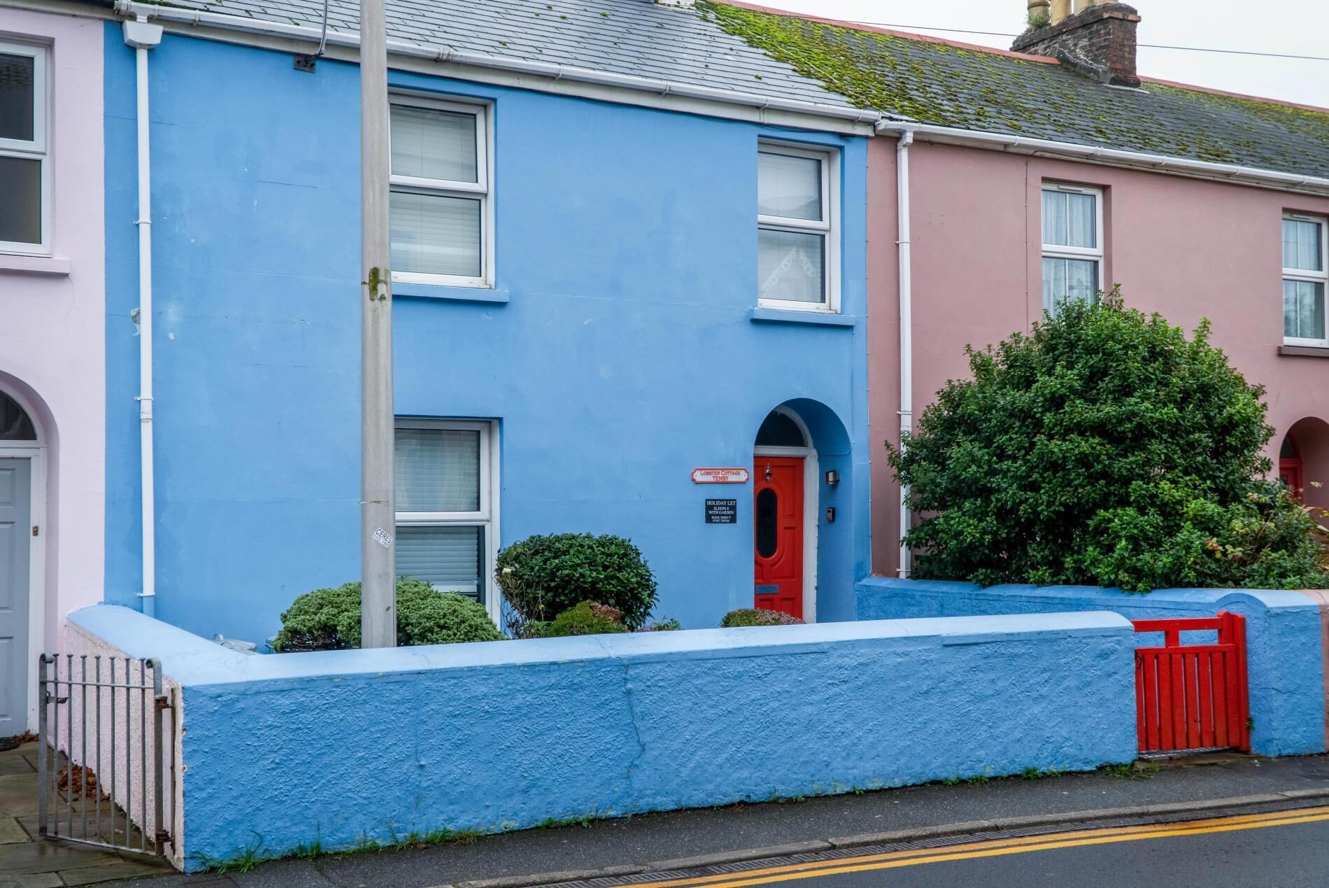 A two-story building with a red door and a sign indicating 'Holiday Let'.