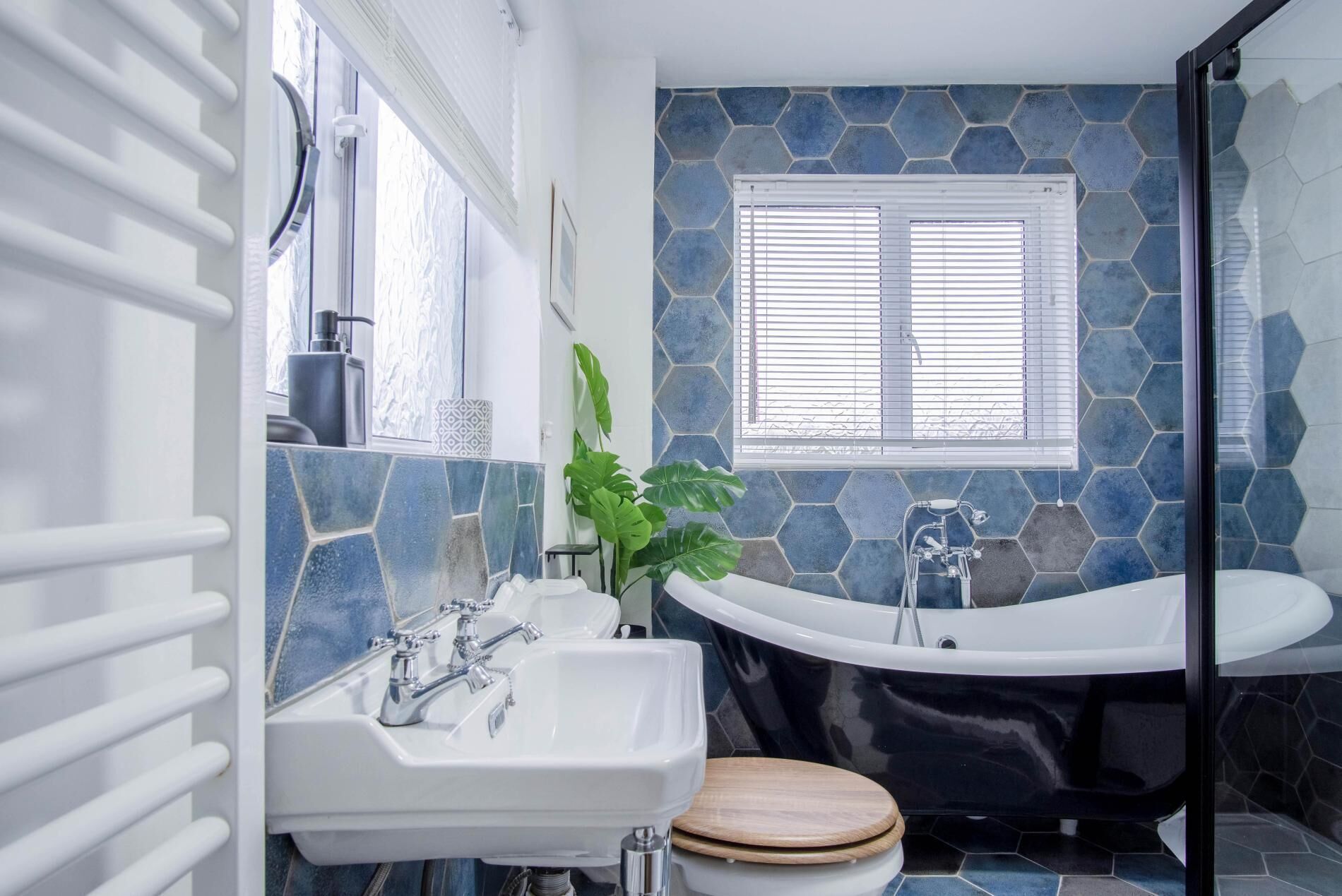 A bathroom with a white sink, a wooden toilet, a freestanding bathtub, and a window with blinds.