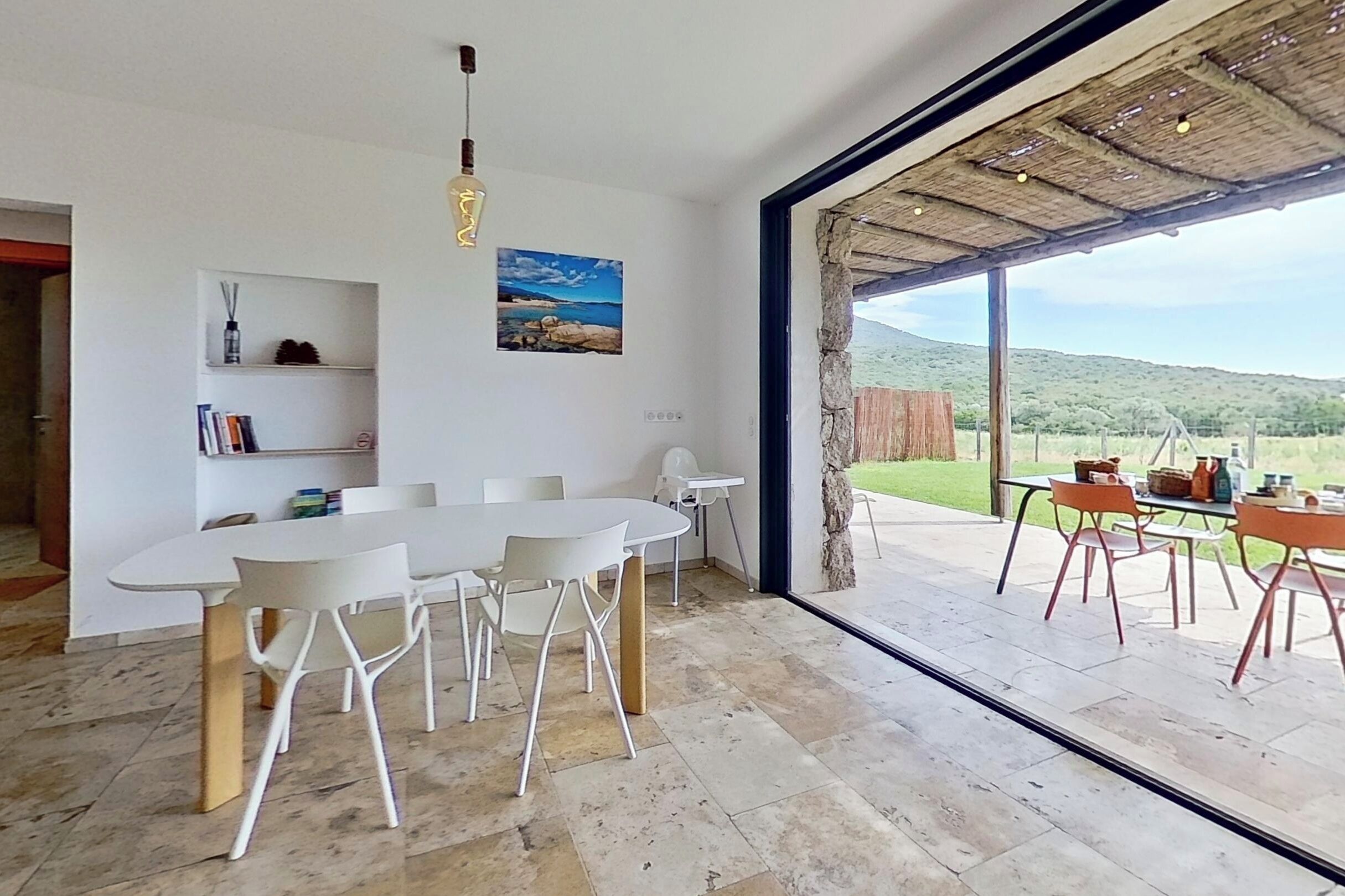 A spacious dining area with a large table and chairs, a hanging light fixture, and a view of the outdoors.