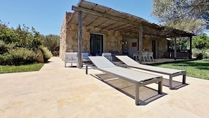 Un bâtiment en pierre doté d’un patio couvert, de chaises longues et de mobilier d’extérieur.