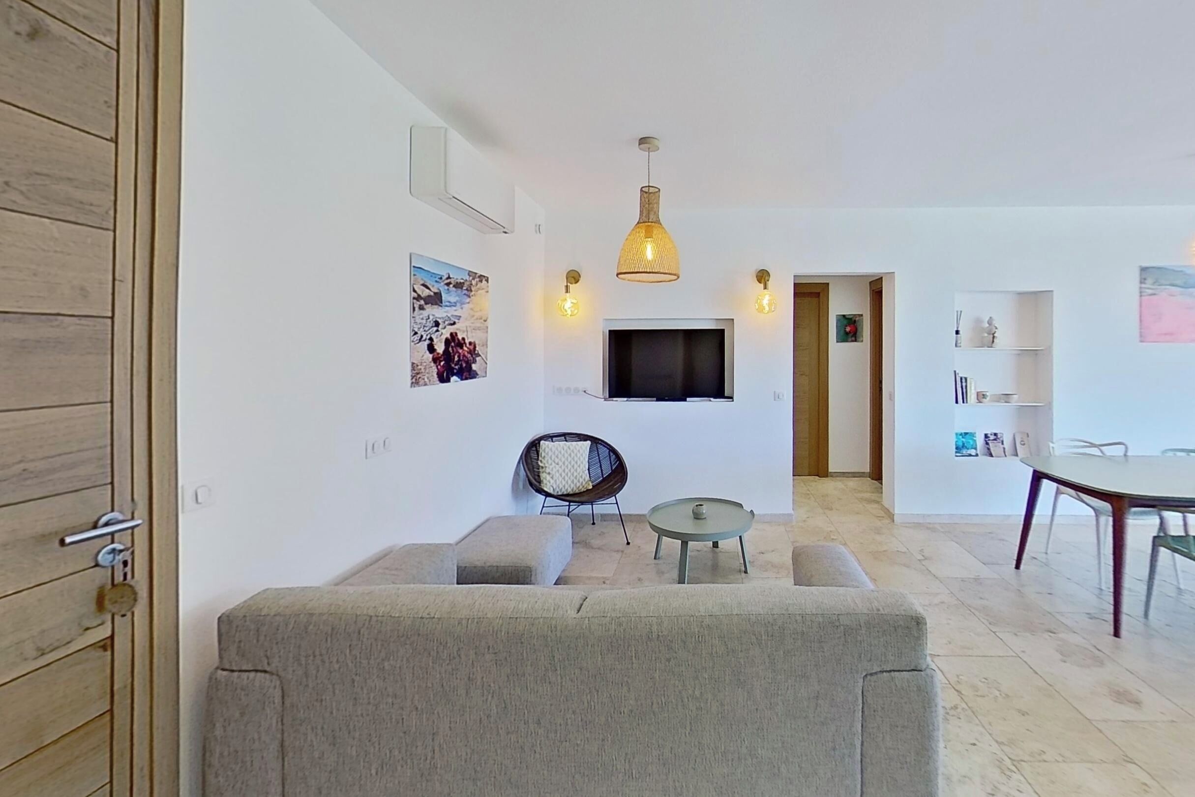 Ein modernes Wohnzimmer mit einer Couch, einem runden Tisch, einem Sessel, einem Fernseher und einer Pendelleuchte.