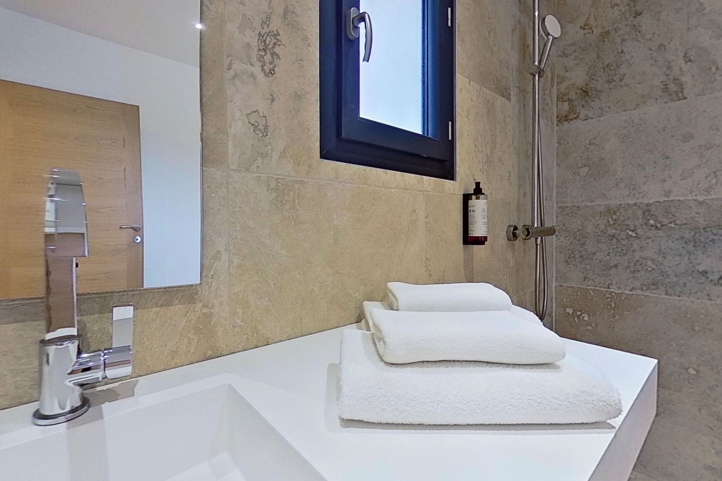 Een moderne badkamer met een wit wastafel, een spiegel, een douche en een handdoekrek.