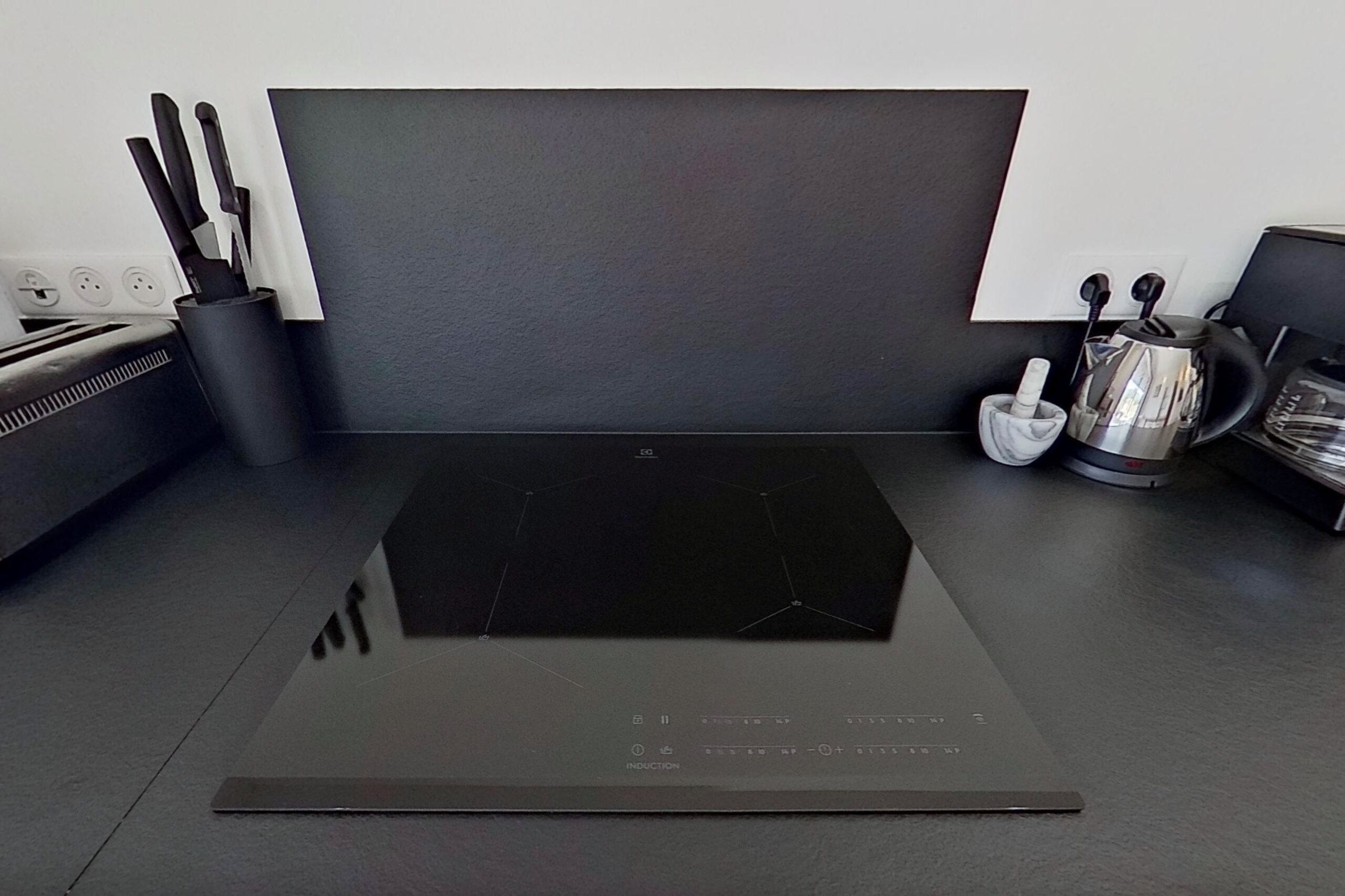 A modern kitchen with a black induction cooktop, a coffee maker, and a knife holder.