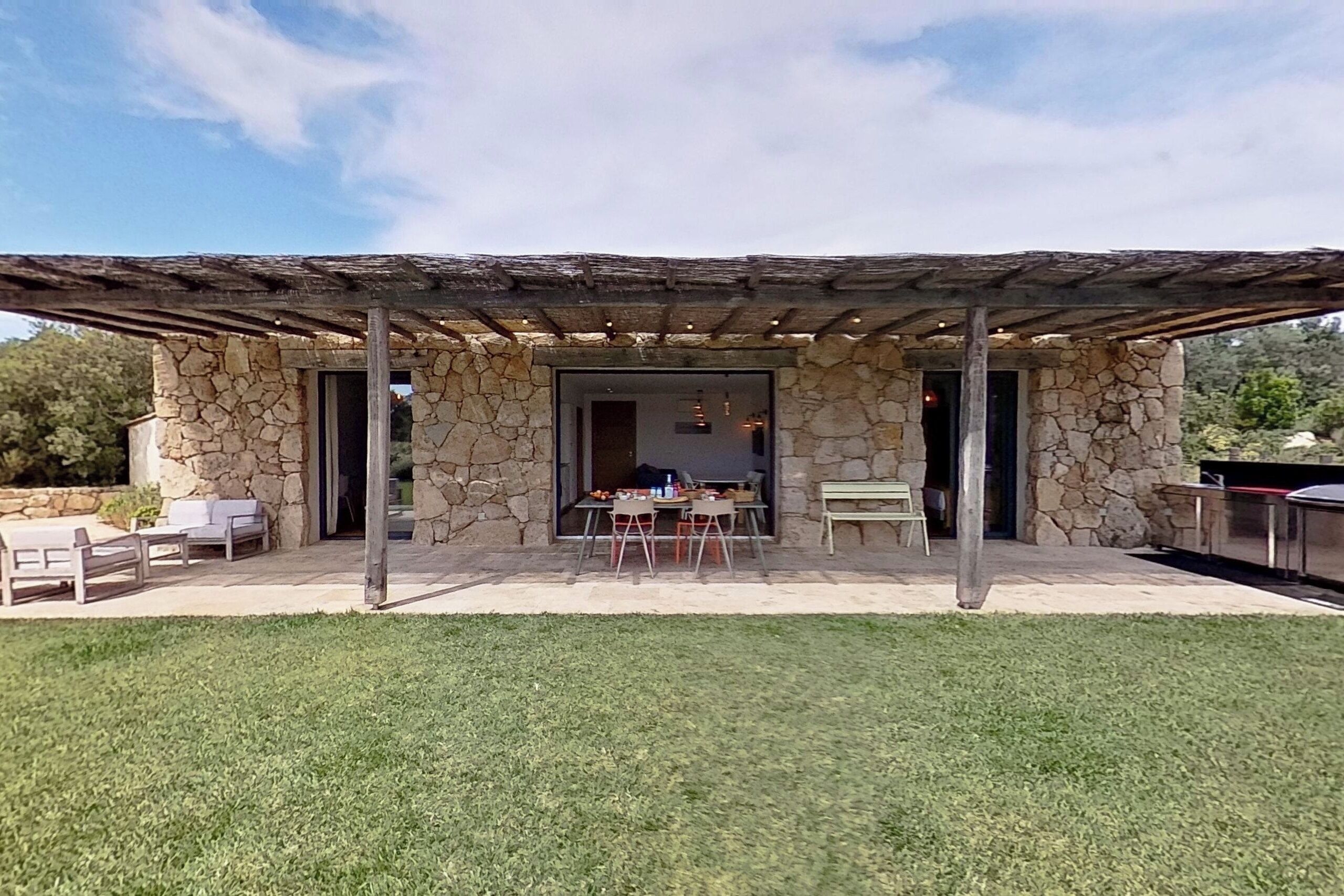 Ein Steinhaus mit überdachter Terrasse, Sitzgelegenheiten im Freien und Grillplatz.