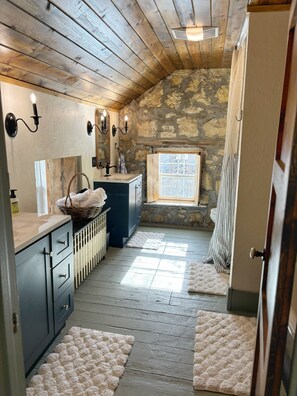 Un baño rústico con paredes de piedra, techo de madera y una ventana que proporciona luz natural.