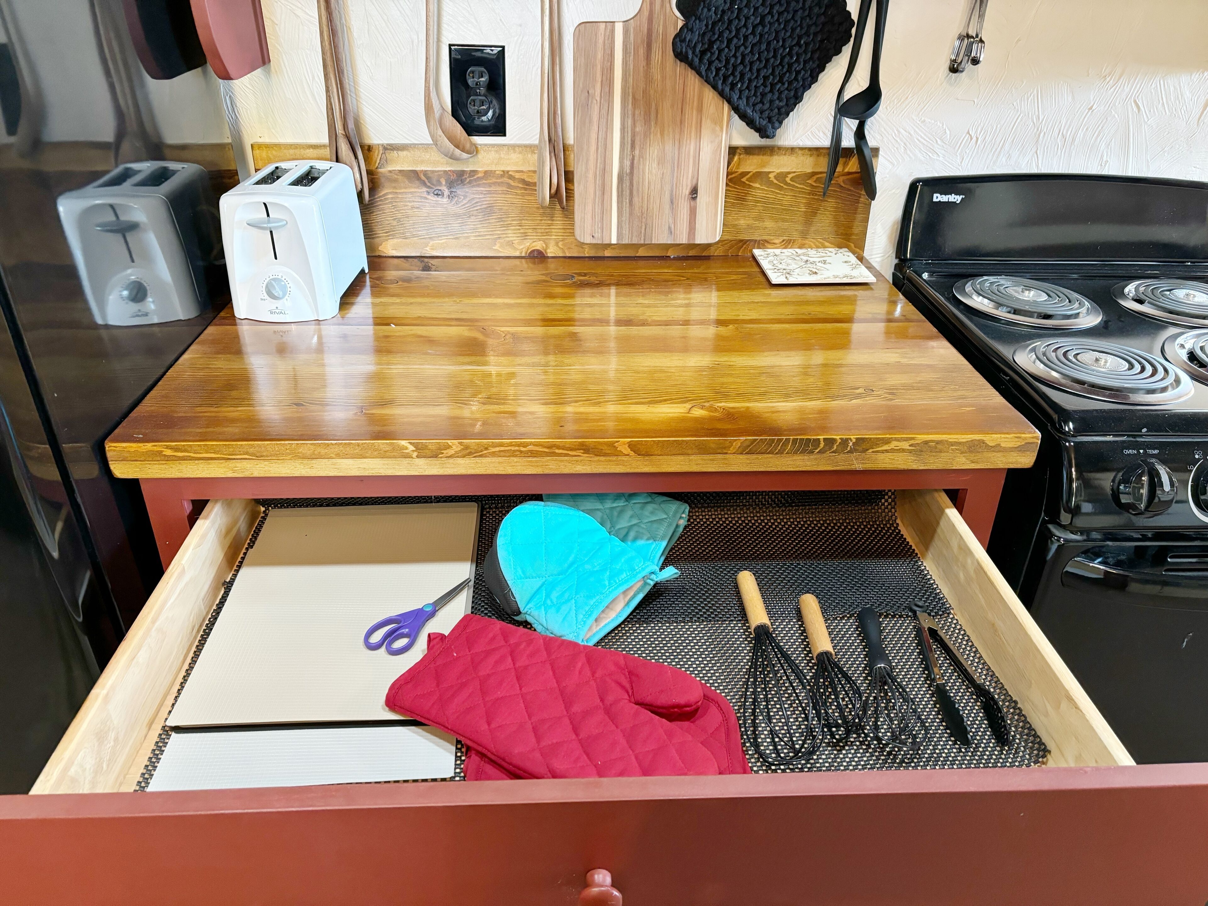 A kitchen with a wooden countertop, a toaster, a cutting board, and a stove.