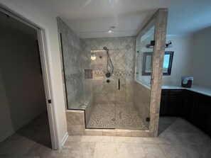 A modern bathroom with a glass-enclosed shower, a tiled floor, and a countertop with a sink and mirror.