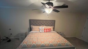 Een slaapkamer met een gestoffeerd hoofdeinde, een bed met een decoratief sprei en een plafondventilator.