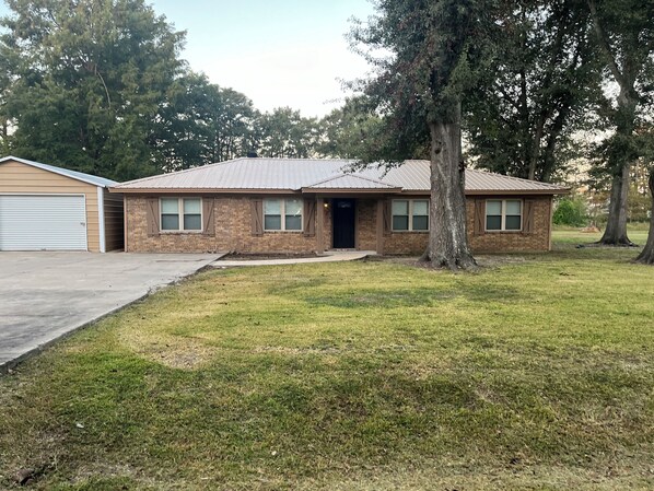 A two-story brick house with a garage, a front yard, and a large tree.