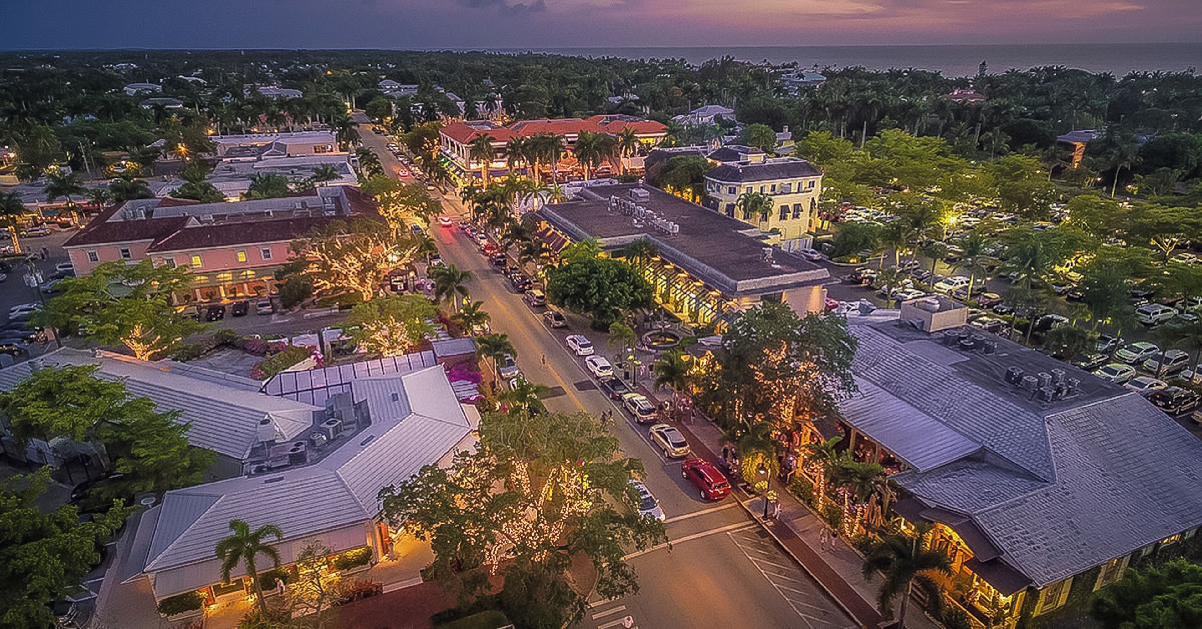 Vue aérienne d’une ville côtière au crépuscule, avec ses bâtiments, ses rues et les voitures garées.