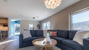 Una sala de estar moderna con un sofá modular gris oscuro, una mesa de centro redonda de madera y una alfombra estampada.