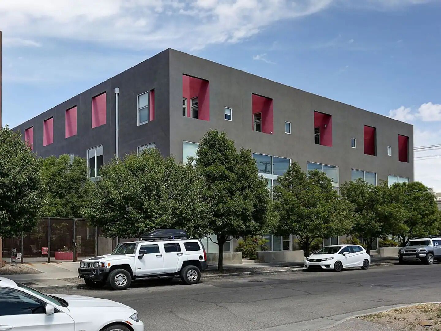 Un edificio moderno con techo plano, ventanas grandes y un estacionamiento con varios coches.