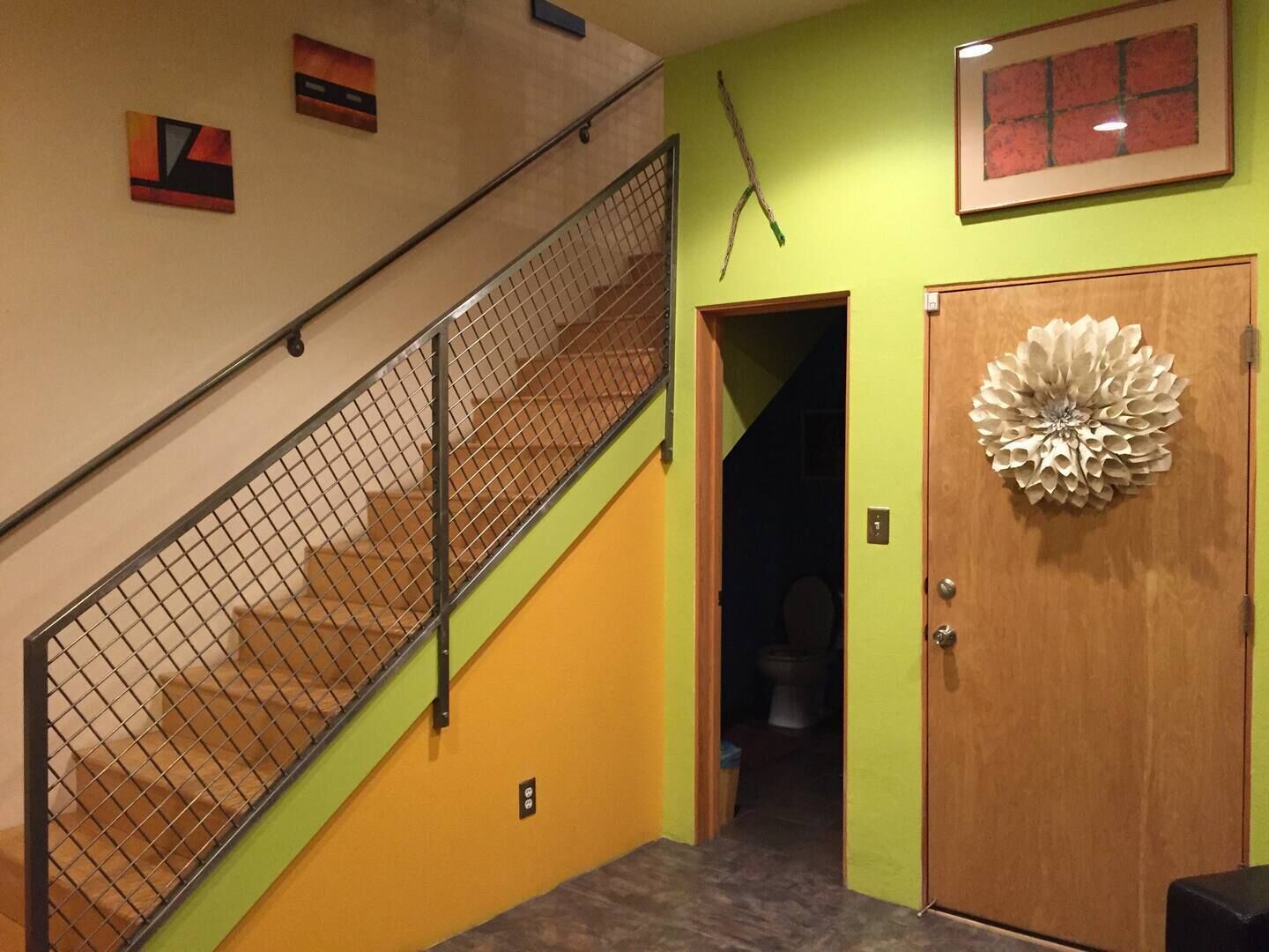 A staircase with a metal railing, a wooden door with a decorative floral design, and a small window with a red frame.