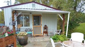 A covered patio area with outdoor seating, a wooden deck, and a garden with potted plants and flowers.